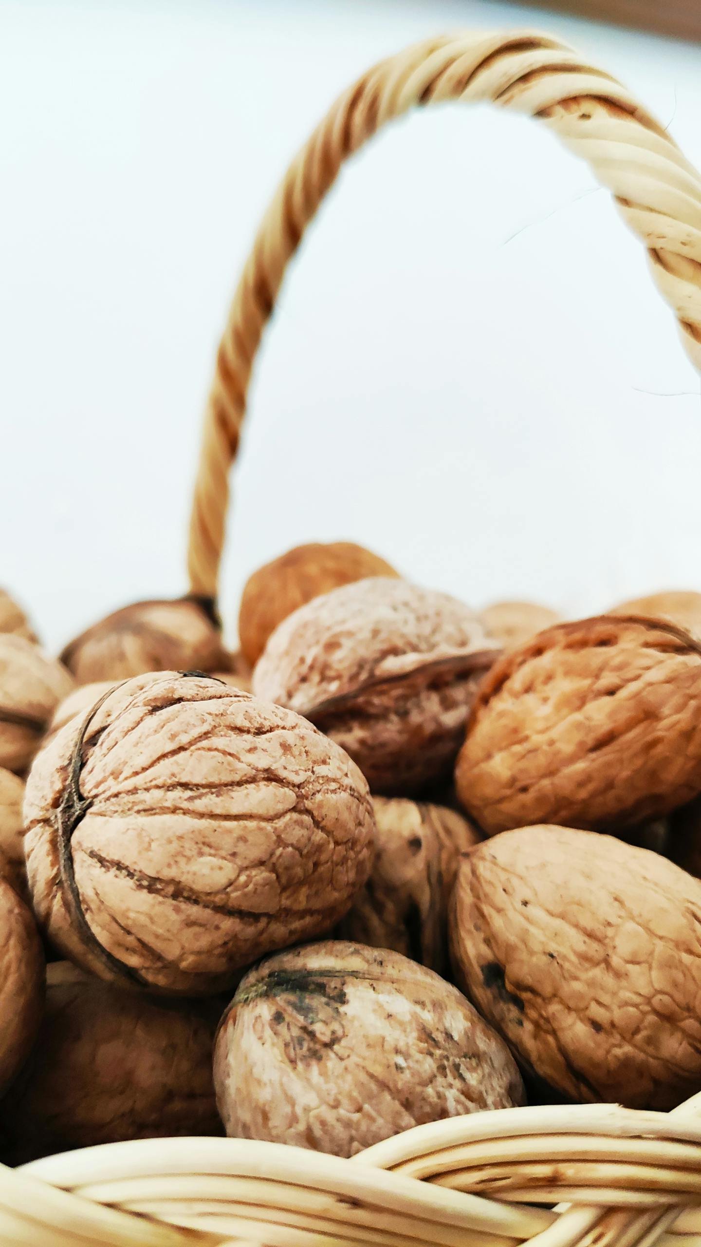 A detailed view of walnuts nested in a woven basket with a light background.
